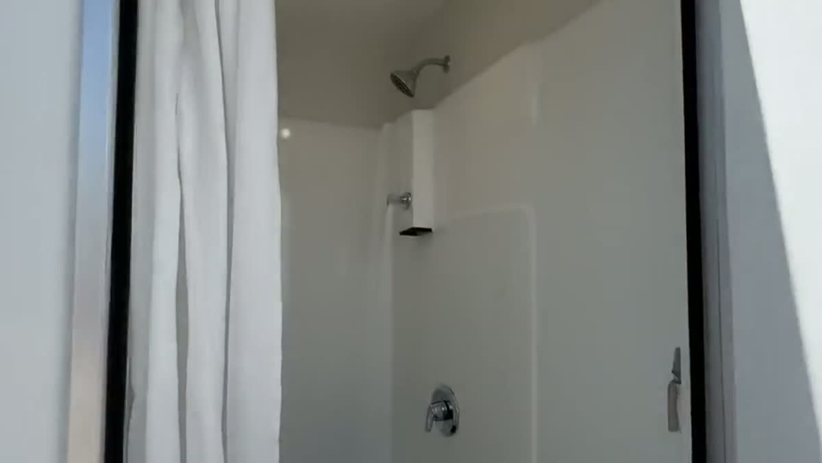Inside a mobile shower trailer, showing a private stall, tiled walls and a lit vanity
